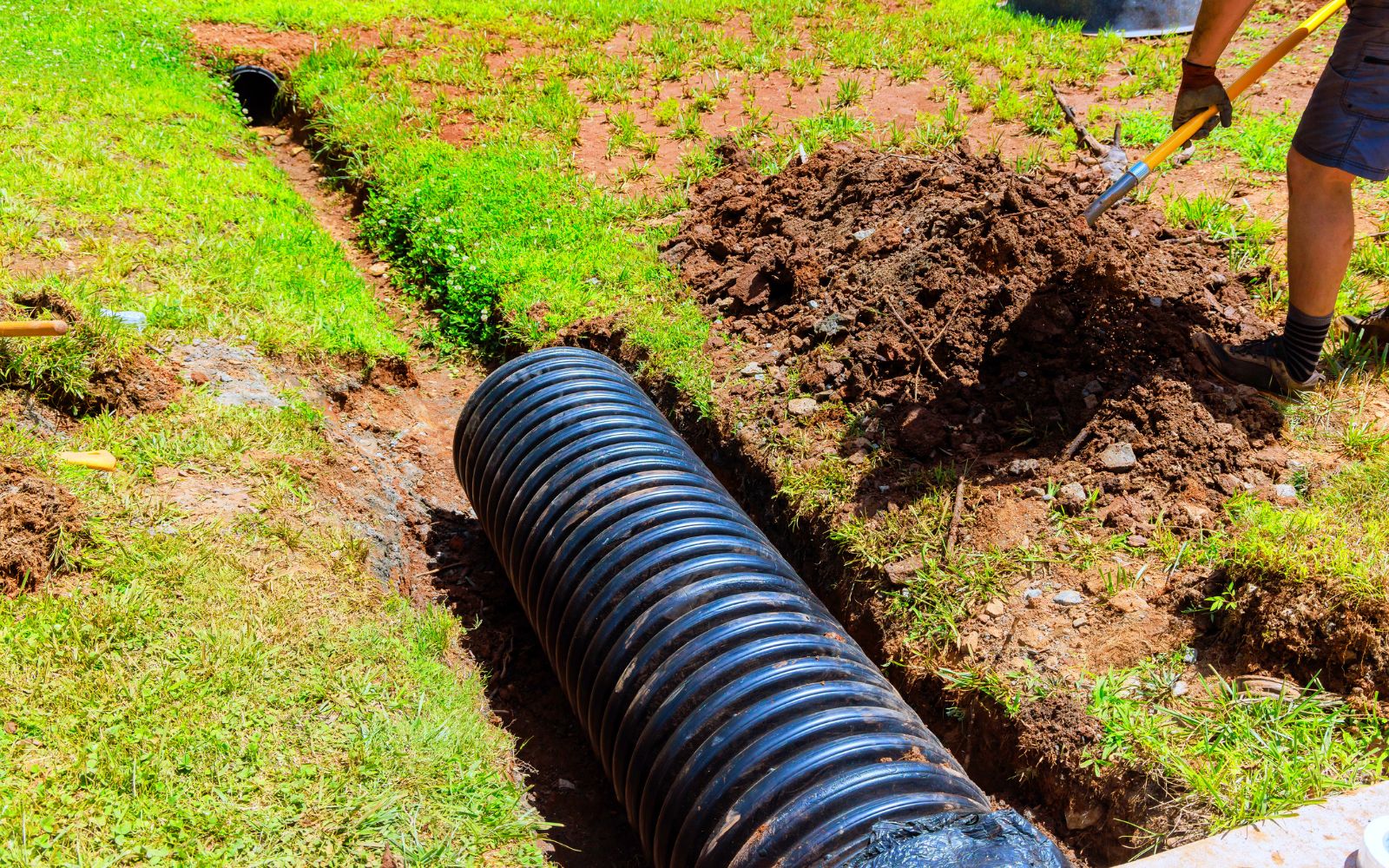 Land drainage solution with trench and rocks to direct water flow away from a lawn and prevent pooling