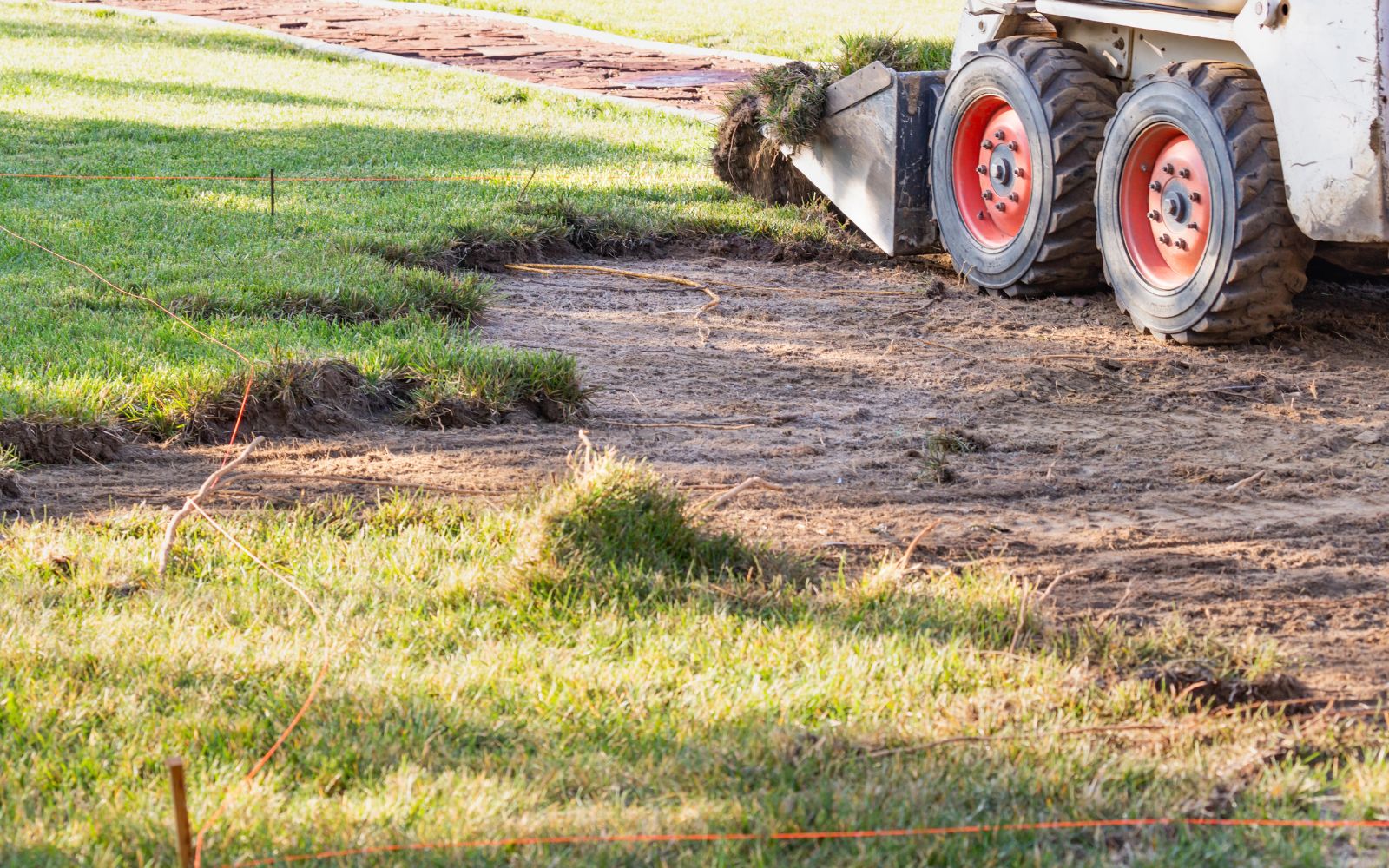 Skid steer performing grading and site preparation on a residential lawn.