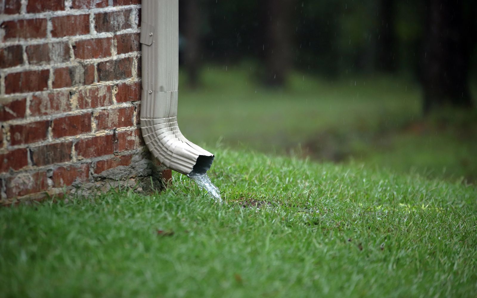 Gutter and downspout drainage system directing roof water away from foundation with landscaping rock bed.