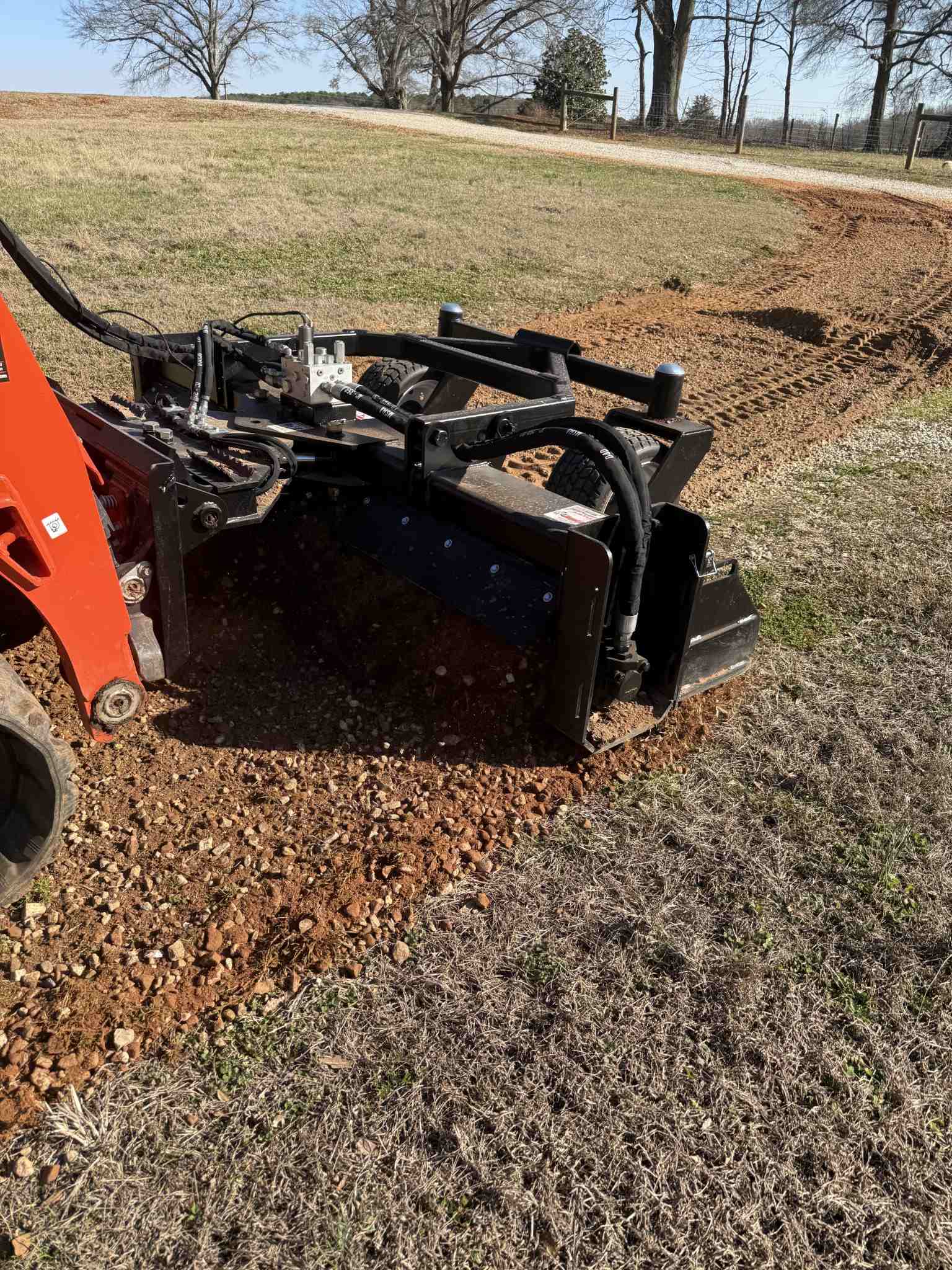 Close-up of a land plane attachment leveling and smoothing uneven gravel on a rural driveway.