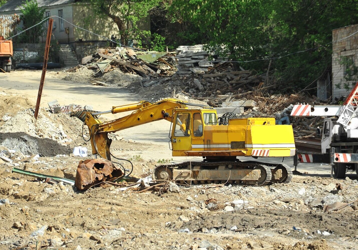 Excavator clearing and reshaping soil at a property edge to prepare the ground for landscaping or groundwork